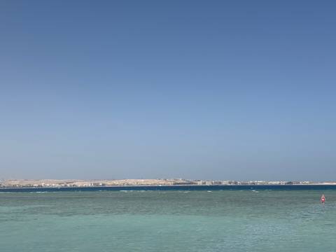 Calm turquoise waters of the Red Sea stretch toward a distant desert shoreline under a clear sky.