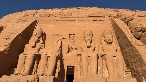 Colossal seated statues of Abu Simbel carved into desert cliff face glow in warm light.