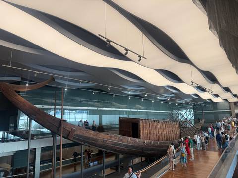 Museum hall exhibits the restored ancient wooden solar boat beneath wave-like ceiling panels.