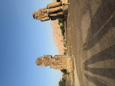 Two giant Colossi of Memnon stand solitary against a barren plain and distant hills.