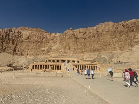 Visitors ascend the grand ramp toward Hatshepsut’s temple carved into towering limestone cliffs.