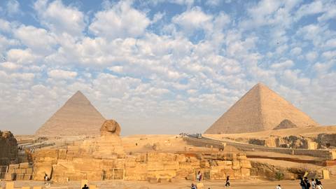 Panoramic view of the Great Pyramids and Sphinx under a dramatic cloud-studded sky.