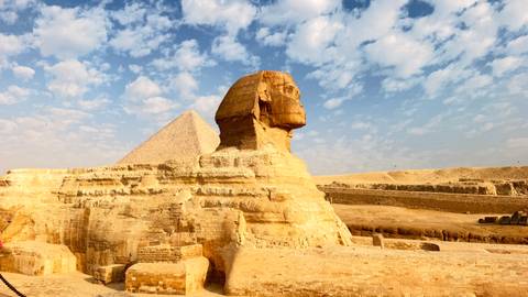 Close-up of the Sphinx profile with pyramid backdrop against a bright sky.