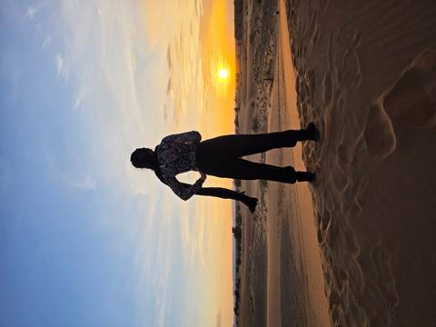 Silhouette of a traveler standing on golden sand dunes watching the sun set over the Sahara.