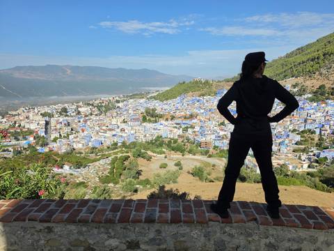 Traveler overlooking the sprawling blue houses of Chefchaouen from a high scenic viewpoint with mountains beyond.