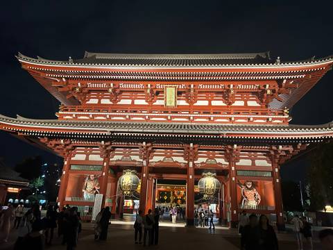 Grand red Kaminarimon gate of Senso-ji temple brightly lit at night with visitors below.