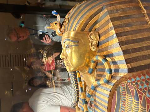 Visitors peer through glass at the golden funerary mask of Tutankhamun in a museum display.