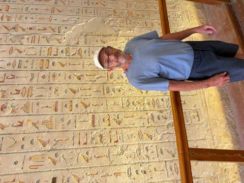 Man stands before a wall densely covered with colorful ancient Egyptian hieroglyphs.
