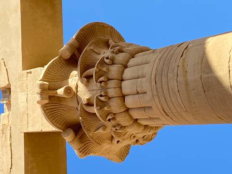 Close-up of an ancient Egyptian lotus capital column against a vivid blue sky.