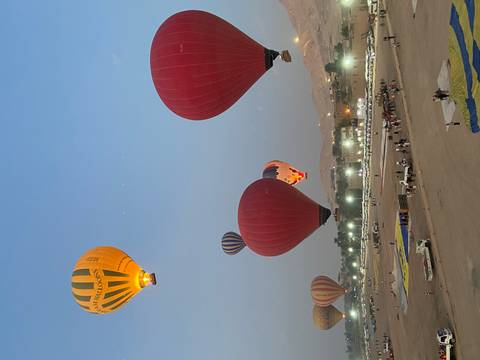 Multiple colorful hot-air balloons ascending over Luxor at dawn with desert hills in the background.