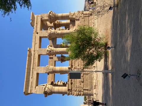 Sandstone colonnade ruins of an ancient riverside temple under a clear blue sky.