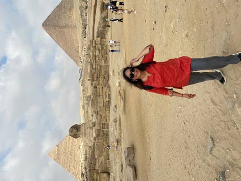 Smiling traveler in front of the Sphinx with pyramids rising behind on a partly cloudy day.