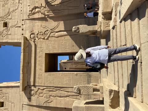 Traveler stands before hieroglyph-covered entrance of Philae Temple complex on a sunny day.