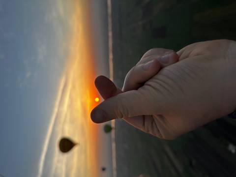 Hand making a heart gesture with sunrise and distant hot-air balloons above the Nile valley.