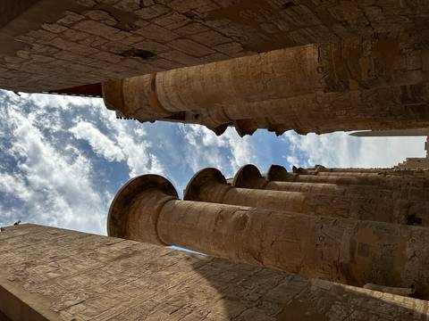 Towering sandstone columns of Karnak Temple frame a distant obelisk under a textured sky.