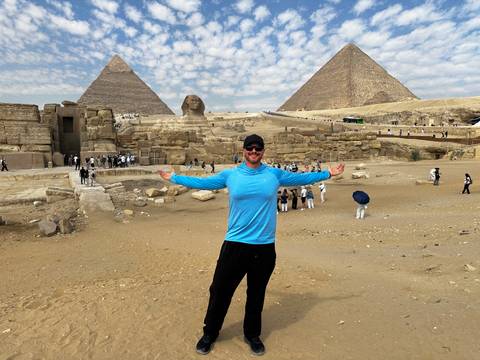 Traveler spreads arms in front of the Sphinx and pyramids under a patterned sky.