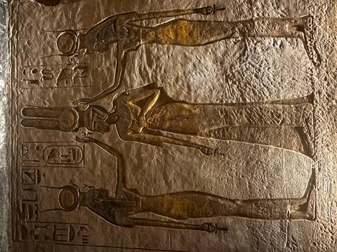 Close-up of gilded wall relief depicting Egyptian deities with hieroglyphic inscriptions.