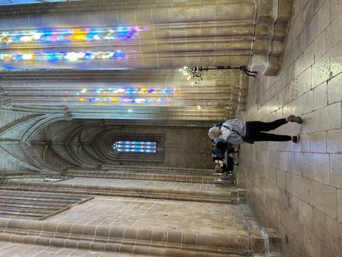 Visitor walking inside a soaring Gothic cathedral lit by colourful stained-glass reflections