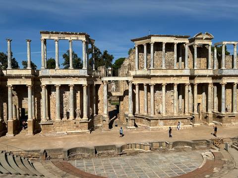 Wide view of the well-preserved Roman theatre with colonnaded stage and people exploring the site