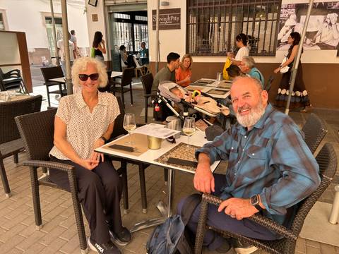 Relaxed outdoor café scene with diners, wine glasses and a baby stroller on a sunny day