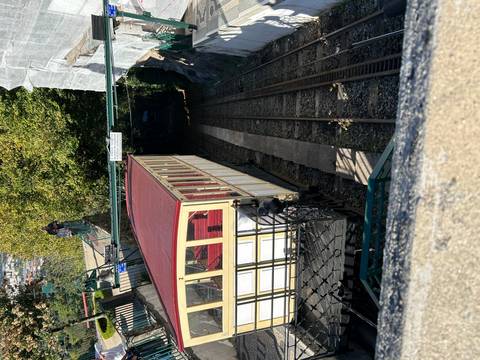 Historic yellow funicular car descending a steep track through a leafy park setting