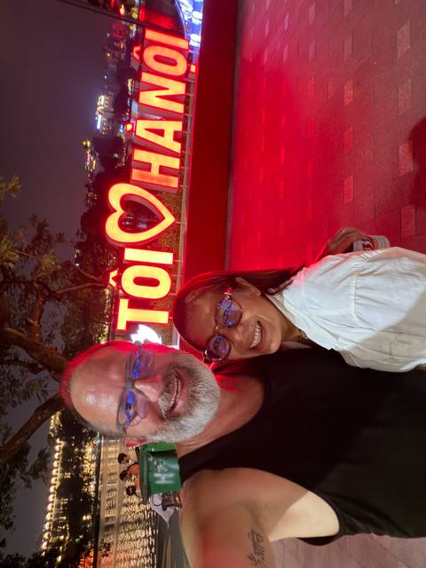 Smiling couple take a closeup selfie at night in front of a bright red neon sign in Vietnam.