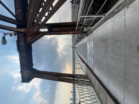 A long concrete lane for motorbikes stretches across a steel bridge arching over a broad river as rays of sunlight break through dramatic afternoon clouds.