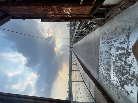 A perspective view down the deck of a historic bridge with moody skies and crepuscular rays shining over the river below.