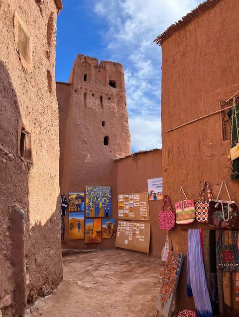 Adobe alleyway lined with colourful local crafts near an ancient mud-brick tower