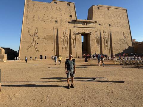 Visitor standing in front of monumental Edfu Temple gate adorned with reliefs