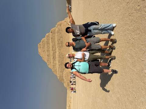 Four travelers pose arm-in-arm in front of the Step Pyramid of Saqqara on a bright desert day.