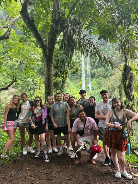 Group of travelers posing in front of a tall jungle waterfall surrounded by lush greenery.