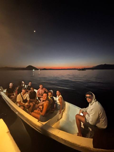 Small boat of travelers at dusk with colorful sunset horizon over calm sea.