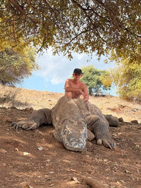 Traveler crouching behind a massive Komodo dragon in a dry savanna landscape.
