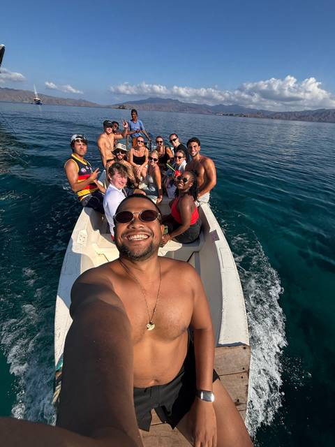Happy group selfie on a small boat speeding over clear blue water.