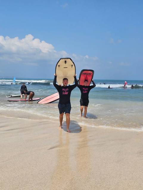 Two surfers in matching rash vests carry boards from the surf while others practice in the waves behind.