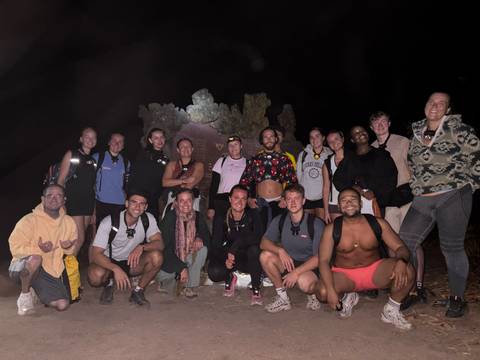 Large hiking group poses at night with head-torches near a rocky formation.