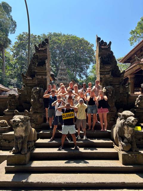 Group copies the hear-no-evil monkey pose at an ornate stone temple entrance filled with carvings.