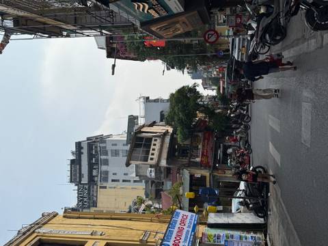 Busy Hanoi street scene with pedestrians, motorbikes, and tall shopfronts under a pale sky.