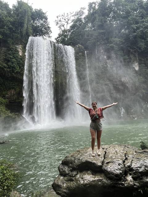 Tilted image of a person posing with arms outstretched near a waterfall.