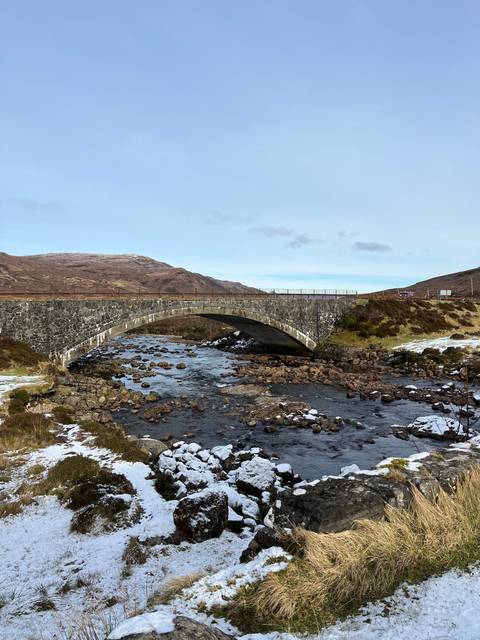 Stone bridge crossing a stream in a snowy landscape.