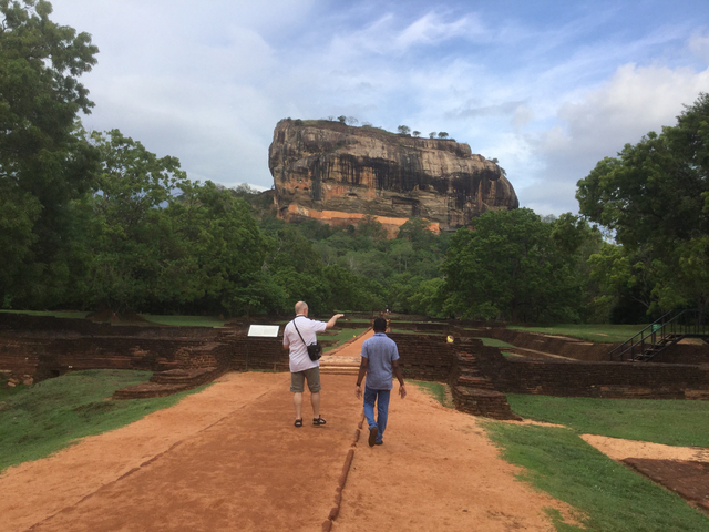 Two people walking towards a large rock formation.