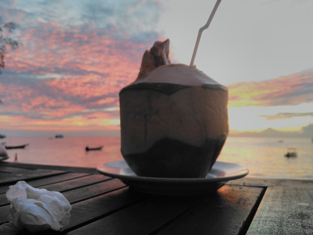 Coconut drink with sunset over the ocean in the background.