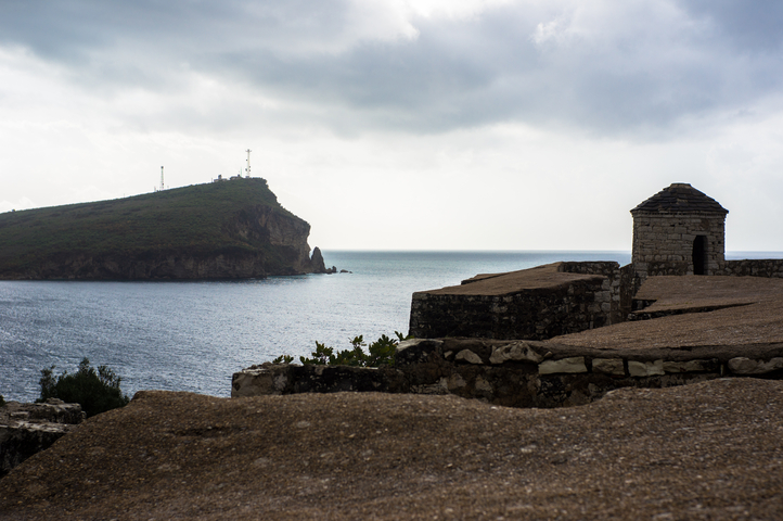 Coastal landscape with rocky cliff and cloudy sky.