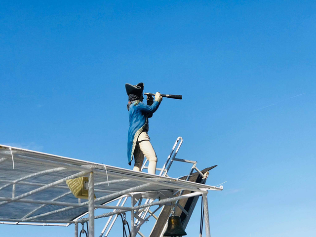 Statue of a naval officer with telescope mounted on a roof against clear blue sky.