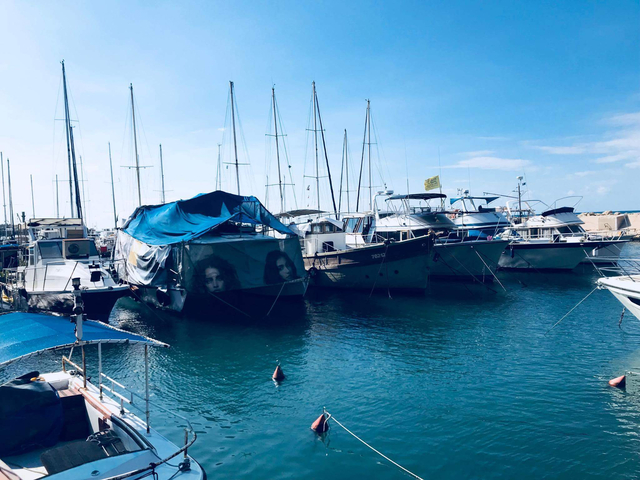 Row of sailboats covered with tarps in a turquoise harbor.