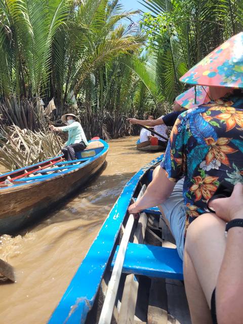 People paddling boats in a narrow waterway surrounded by lush palm trees.