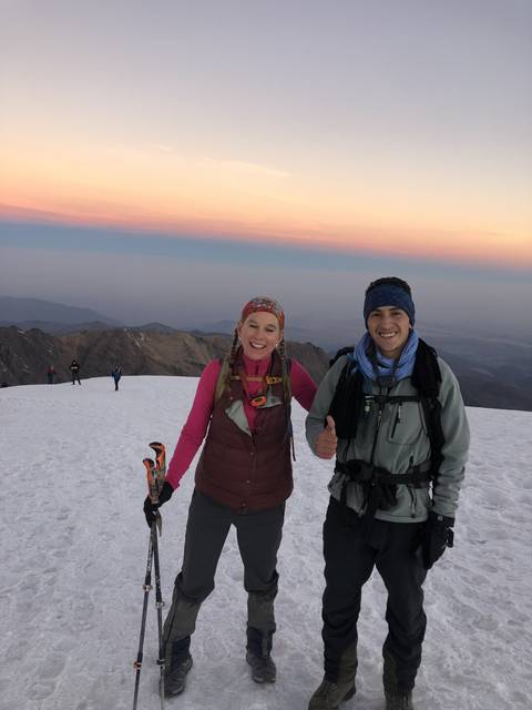 Smiling climbers on a snow-covered mountain at sunset.