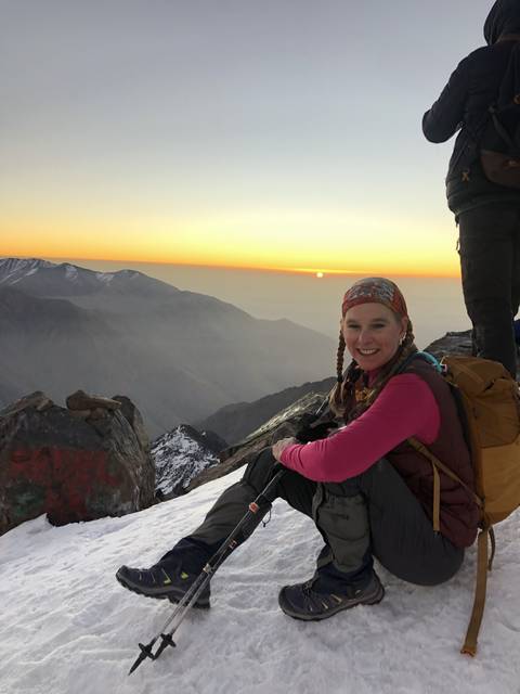 Person squatting on snowy mountain with a summit view.