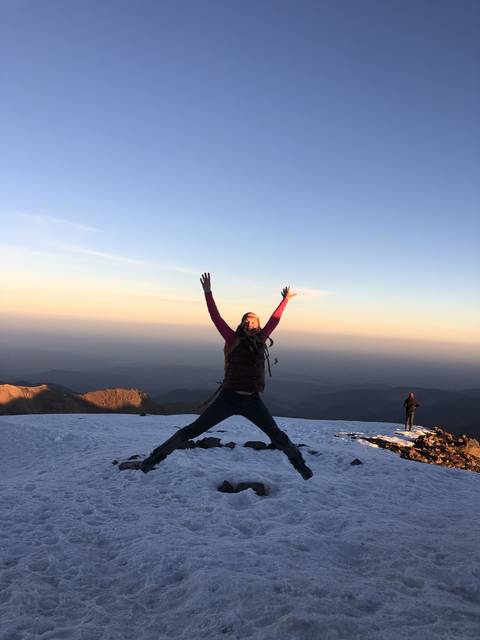 Hiker jumping joyfully on a snowy mountain top.